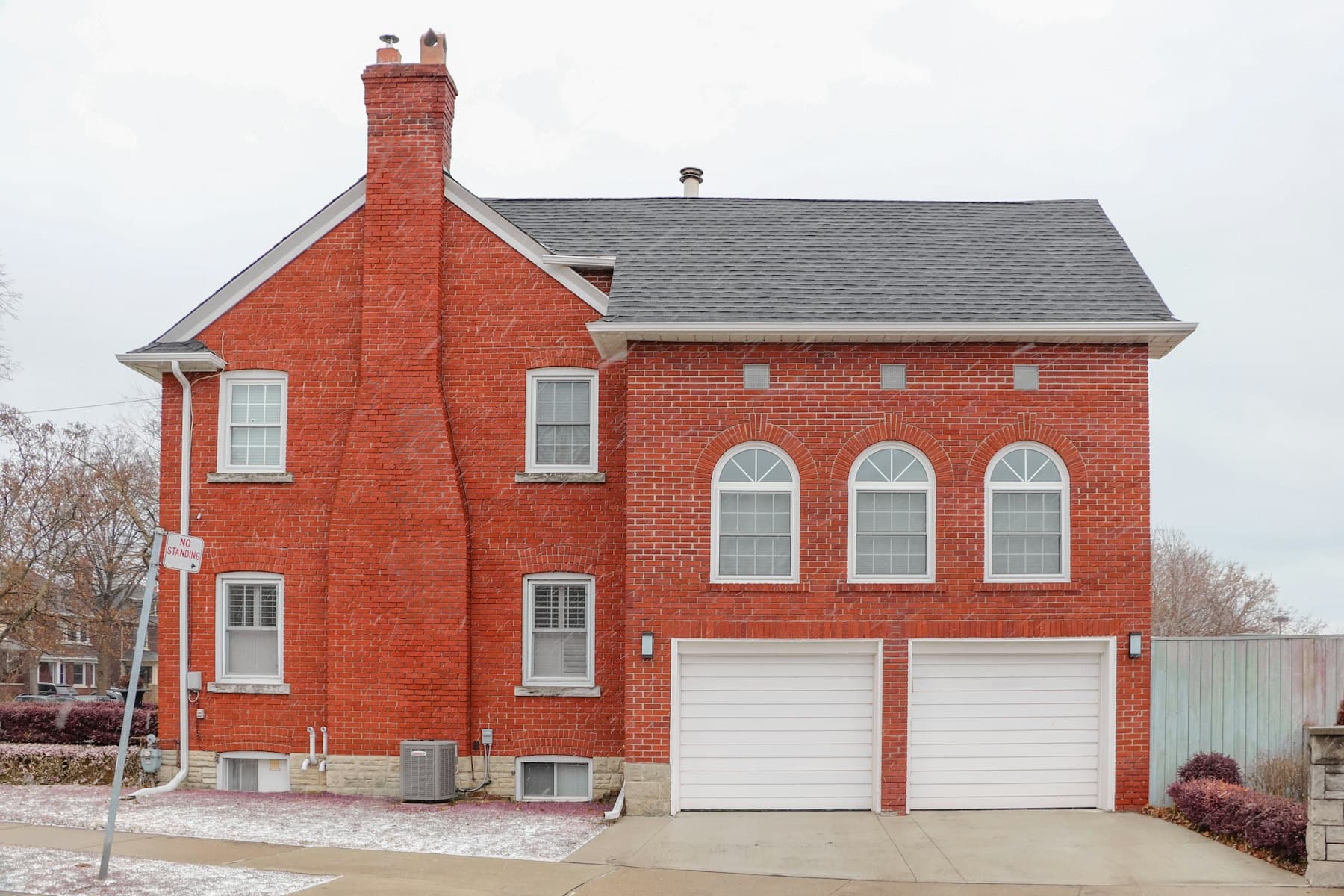 Red brick home with two white garage doors in light snow